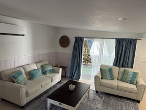 A living room with two sofas, a coffee table, and a view of a decorated Christmas tree through a glass door.