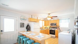 A kitchen with wooden cabinets, a central island with bar stools, a refrigerator, a microwave, and a washing machine.