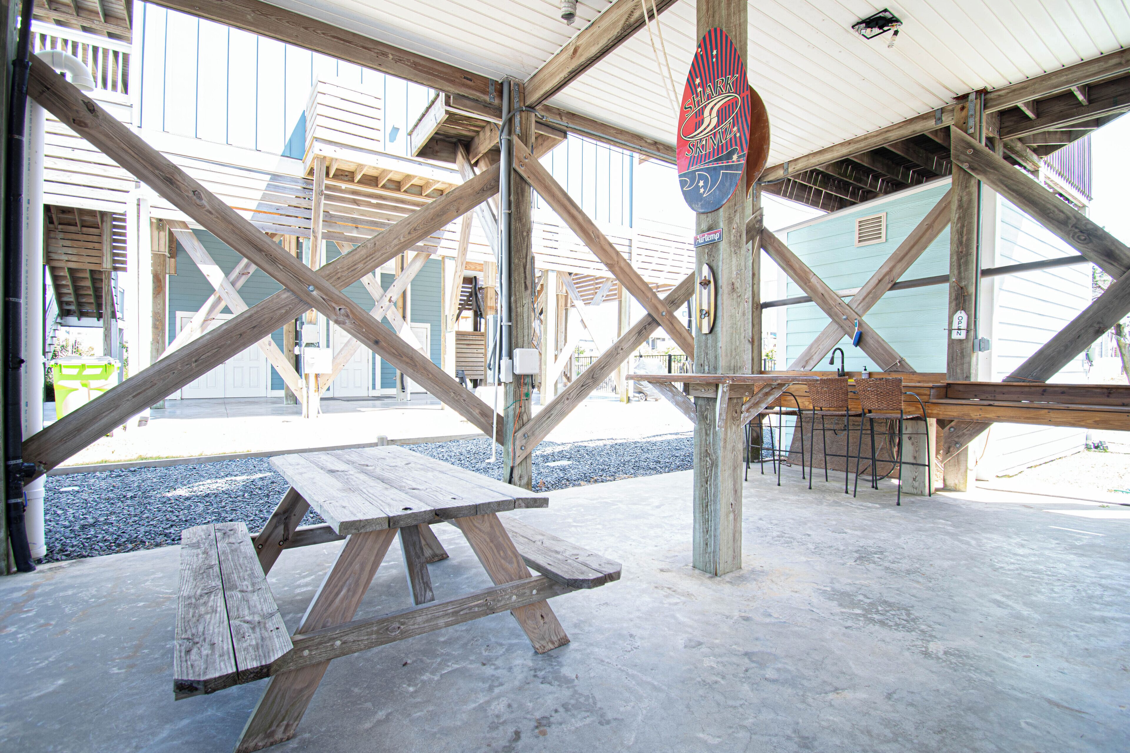 A wooden picnic table and benches under a metal roof structure.