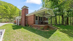 A brick house with a covered porch, a chimney, and a well-maintained lawn.