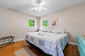 A bedroom with a bed, a ceiling fan, two windows, a deer artwork, a dresser, and a patterned rug.