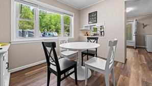 A kitchen with a round table and chairs, a window with blinds, and a door leading to another room.