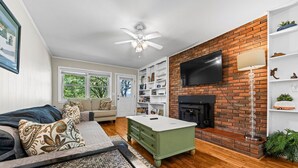 A living room with a sofa, a coffee table, a fireplace, a TV mounted on the wall, and a bookshelf.