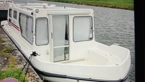 Un petit bateau blanc était amarré à un quai, avec une zone herbeuse et un ciel nuageux en arrière-plan.