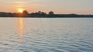 Un lac paisible au coucher du soleil, avec une rive rocheuse et une végétation clairsemée.