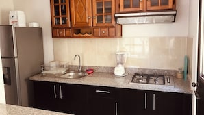 Una cucina con mobili in legno, un piano di lavoro in granito, un frigorifero in acciaio inossidabile, un lavello, un frullatore e una cucina a gas.