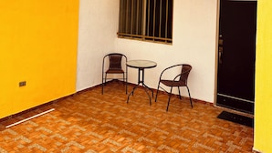 Un piccolo patio con due sedie e un tavolo, una finestra con inferriate e una porta.