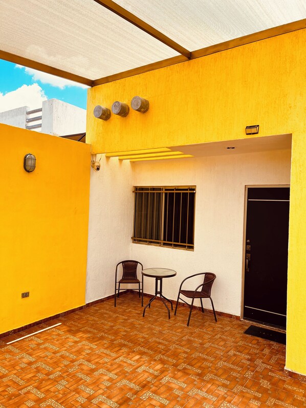 A small patio with two chairs and a table, a window with bars, and a door. - Bonita Casa Vacacional en Las Americas (Mérida)