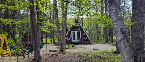 A cabin in a forest with a dirt path leading to it, surrounded by trees.