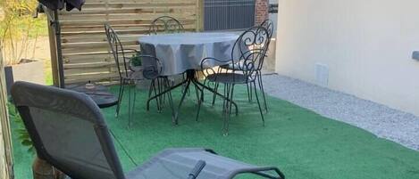 Eine Terrasse mit Tisch, Stühlen und einem überdachten Sonnenschirm, belegt mit Kunstgrasanlage.