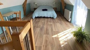 A bedroom with a sloped ceiling, wooden beams, a bed with a blue cover, a small table, and a potted plant.