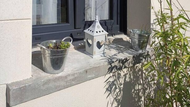 A window with sheer curtains, a small white lantern, and a potted plant on the ledge.