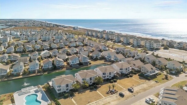 Una zona residencial costera con casas de varios pisos, un puerto deportivo y una playa al fondo.