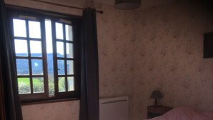 A bedroom with a bed, a window with curtains, a radiator, and a lamp on a bedside table. - House Les Mésanges, Loire valley, nature near Puy en Velay (Saint-Maurice-de-Lignon)