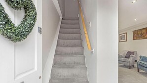 A staircase with grey carpeted steps, a wooden handrail, and a green wreath on the wall.