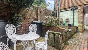 A patio with white metal chairs and a table, a brick wall, and a stone bench.