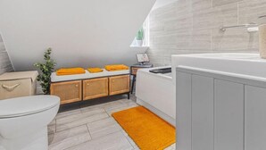 A modern bathroom with a toilet, sink, and bathtub. There is a window providing natural light and a small plant on the windowsill.