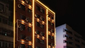 Un edificio de varios pisos con fachada moderna, que presenta una serie de ventanas regularmente espaciadas y una llamativa tira de luz vertical que recorre el borde del edificio.