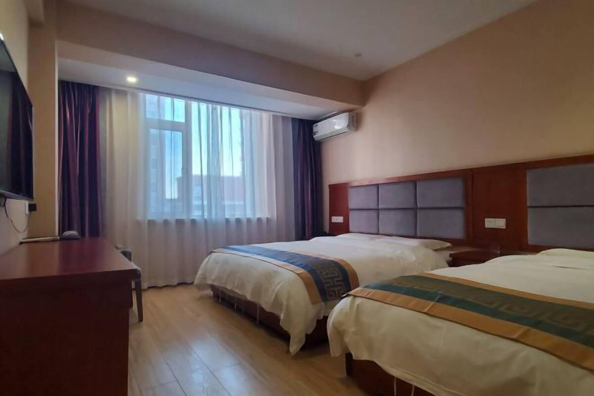 A hotel room with two beds, a desk, and a large window with curtains.