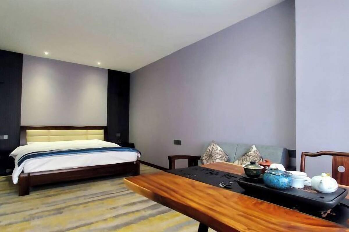 A hotel room with a bed, a wooden table with teapots, and a sofa.