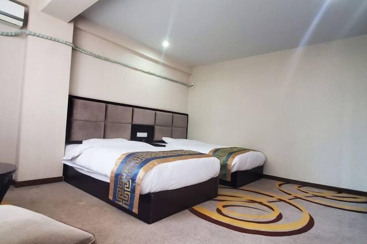 A hotel room with two beds, a headboard, a bedside table, and a carpet with a circular pattern.