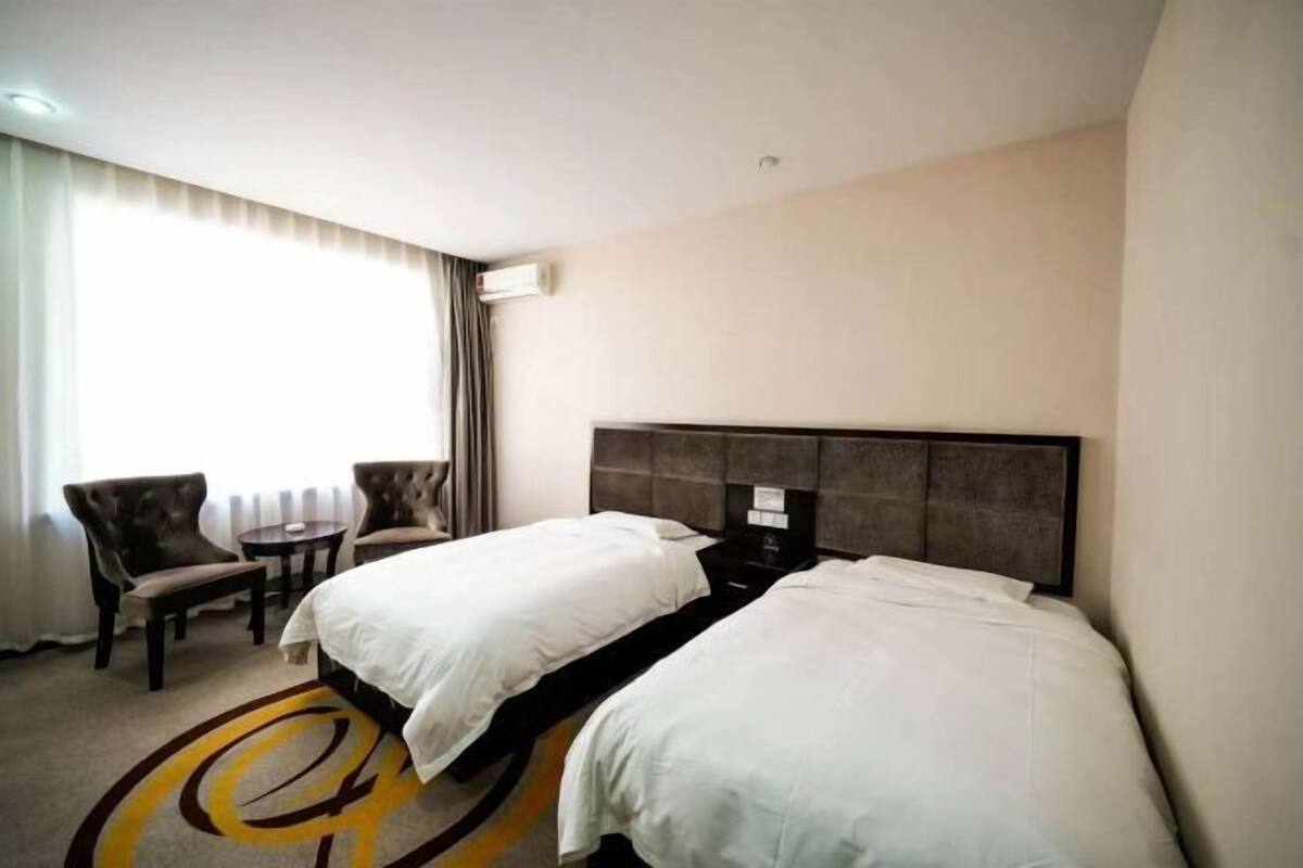 A hotel room with two beds, a small table, two chairs, and a window with curtains.