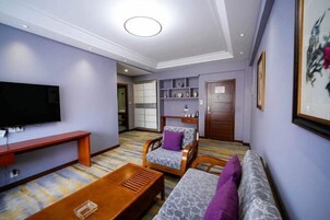 A living room with a flat-screen TV, wooden furniture, a sofa, a chair, and a coffee table.