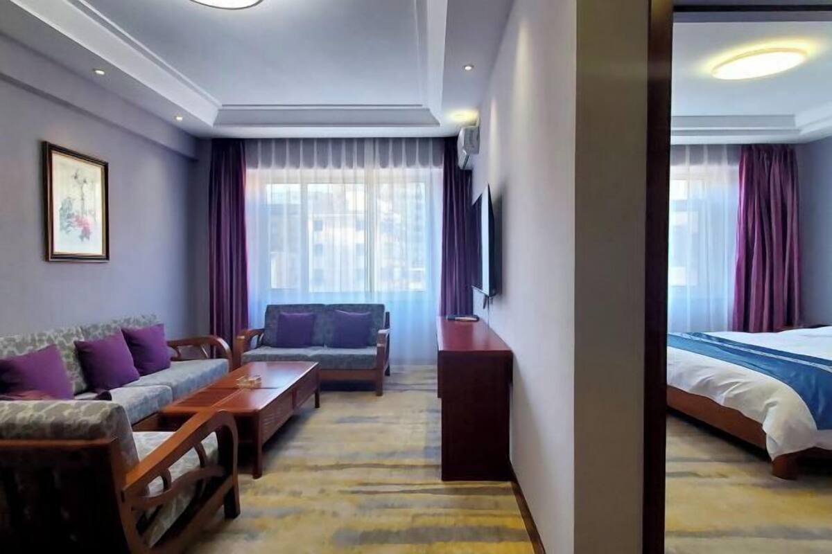 A hotel room with a sofa, a wooden coffee table, a bed, and a TV mounted on the wall.