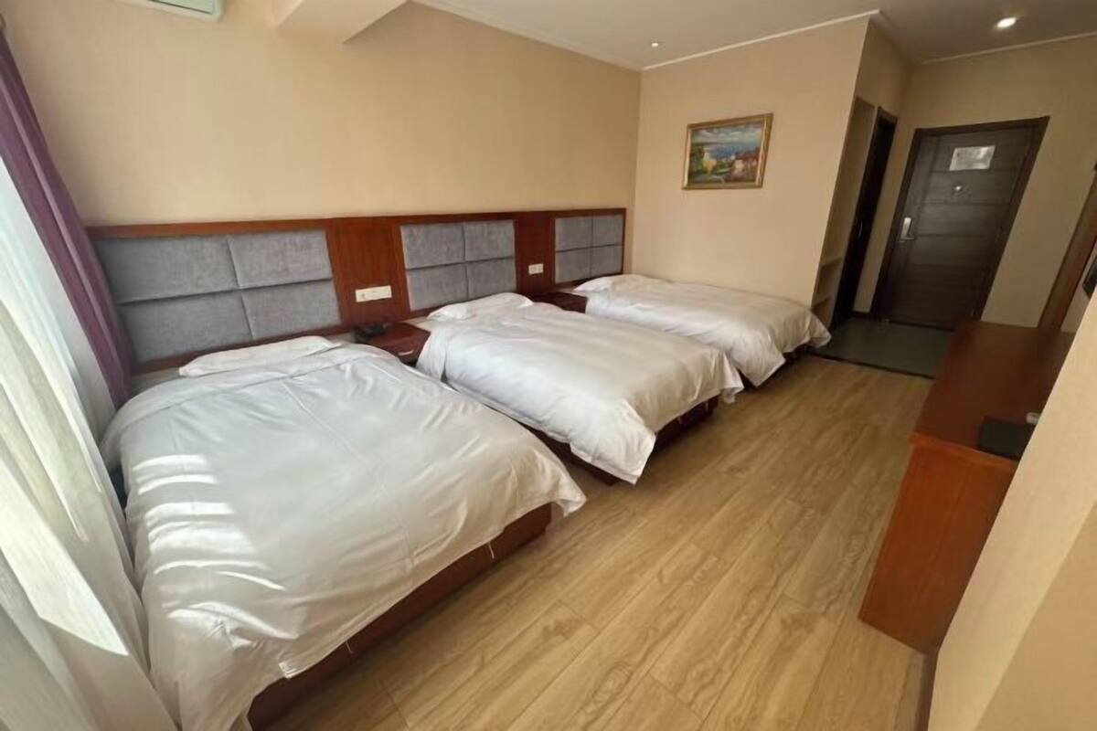 A hotel room with two beds, a wooden headboard, a painting on the wall, and a door.
