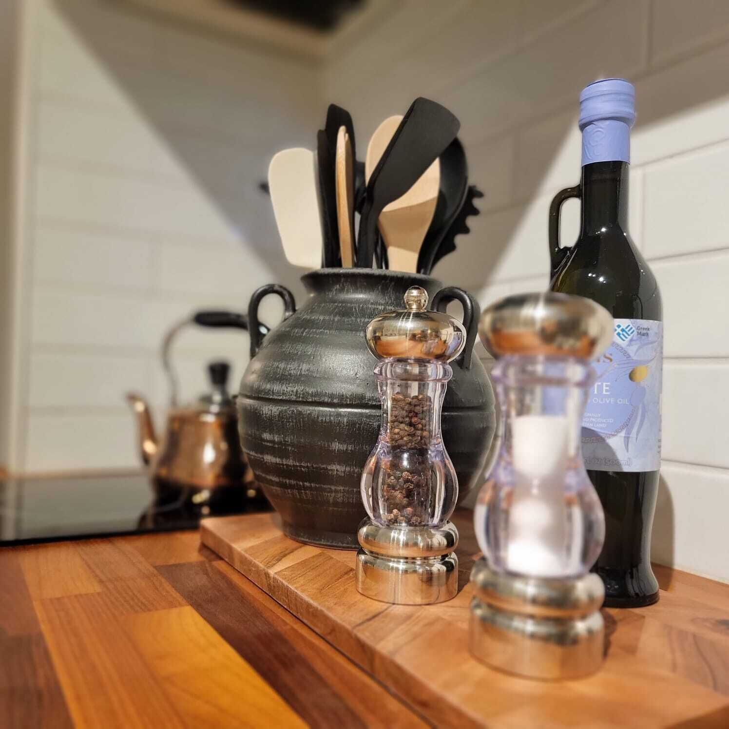 A kitchen counter with a large ceramic pot, a bottle of olive oil, and a pepper grinder.