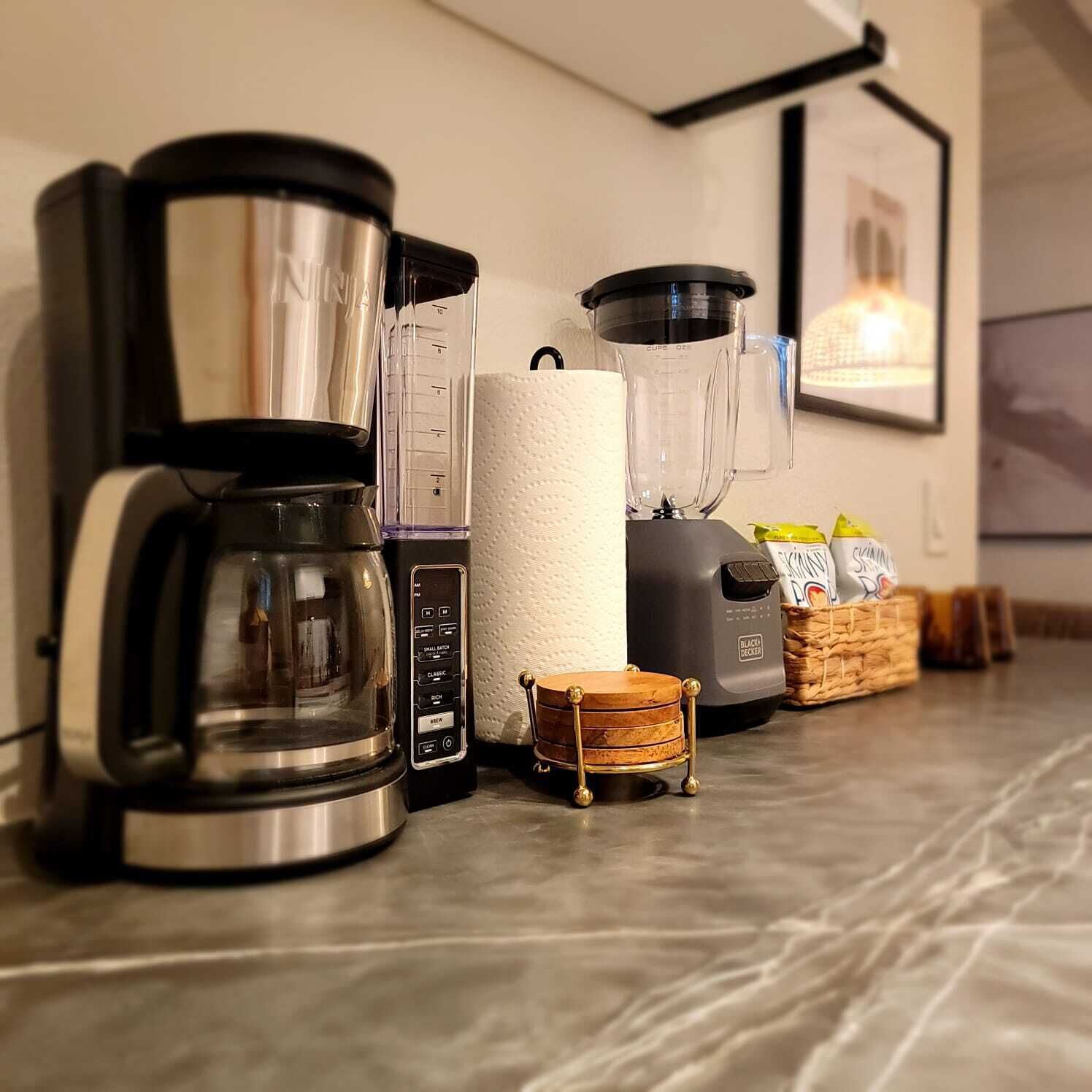 Keittiön työtasolla on kahvinkeitin, tehosekoitin, paperipyyheteline ja kori, jossa on kahvikapseleita.