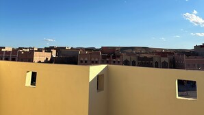 Une terrasse offrant une vue dégagée sur le ciel, avec un mur jaune orné d’une petite fenêtre et une table en métal.