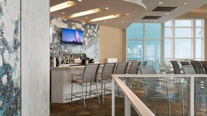Un espace bar moderne avec un téléviseur fixé sur un mur en mosaïque, des tabourets de bar et un coin salon avec des tables et des chaises.