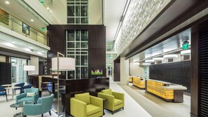 Un vestíbul d'hotel modern amb una zona d'estar central, una recepció i un sostre alt amb il·luminació decorativa.