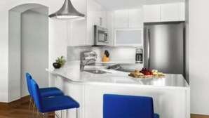 A modern kitchen with white cabinetry, a stainless steel refrigerator, and a central island with blue bar stools.