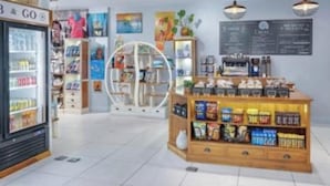 A store interior with a refrigerated section, shelves stocked with snacks, and a coffee bar.