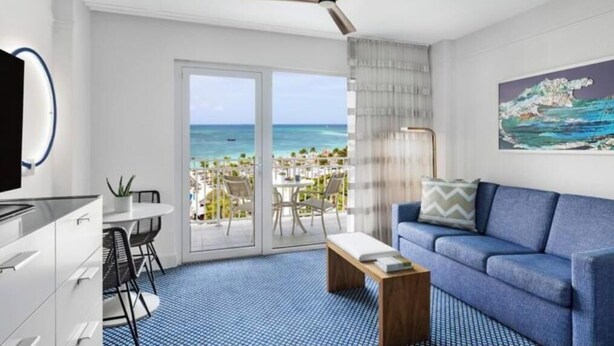 A modern hotel room with a balcony, a dining area, and a living space.