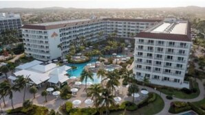 A hotel with multiple floors, a central pool area surrounded by palm trees, and a landscaped garden.
