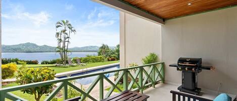 A balcony with a view of a lake and mountains, a barbecue grill, and outdoor seating.