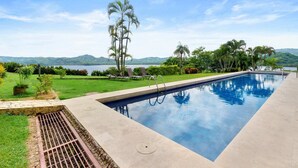 A rectangular swimming pool with a clear blue water surface, surrounded by a well-maintained lawn and palm trees. - Ground-Floor Condo Near Beach & Marina by SPCR (Playa Flamingo)