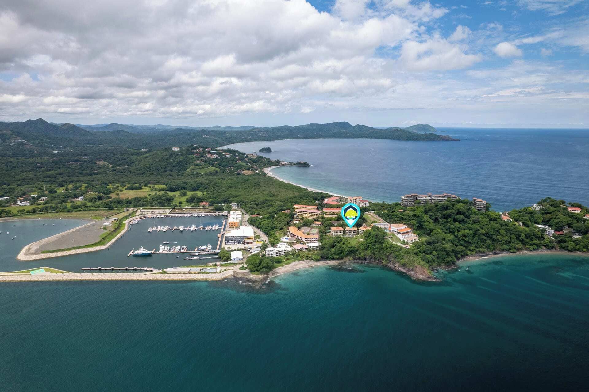 An aerial view of a coastal area with a marina, buildings, and a forested island.