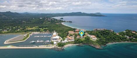 An aerial view of a coastal area with a marina, buildings, and a forested island.
