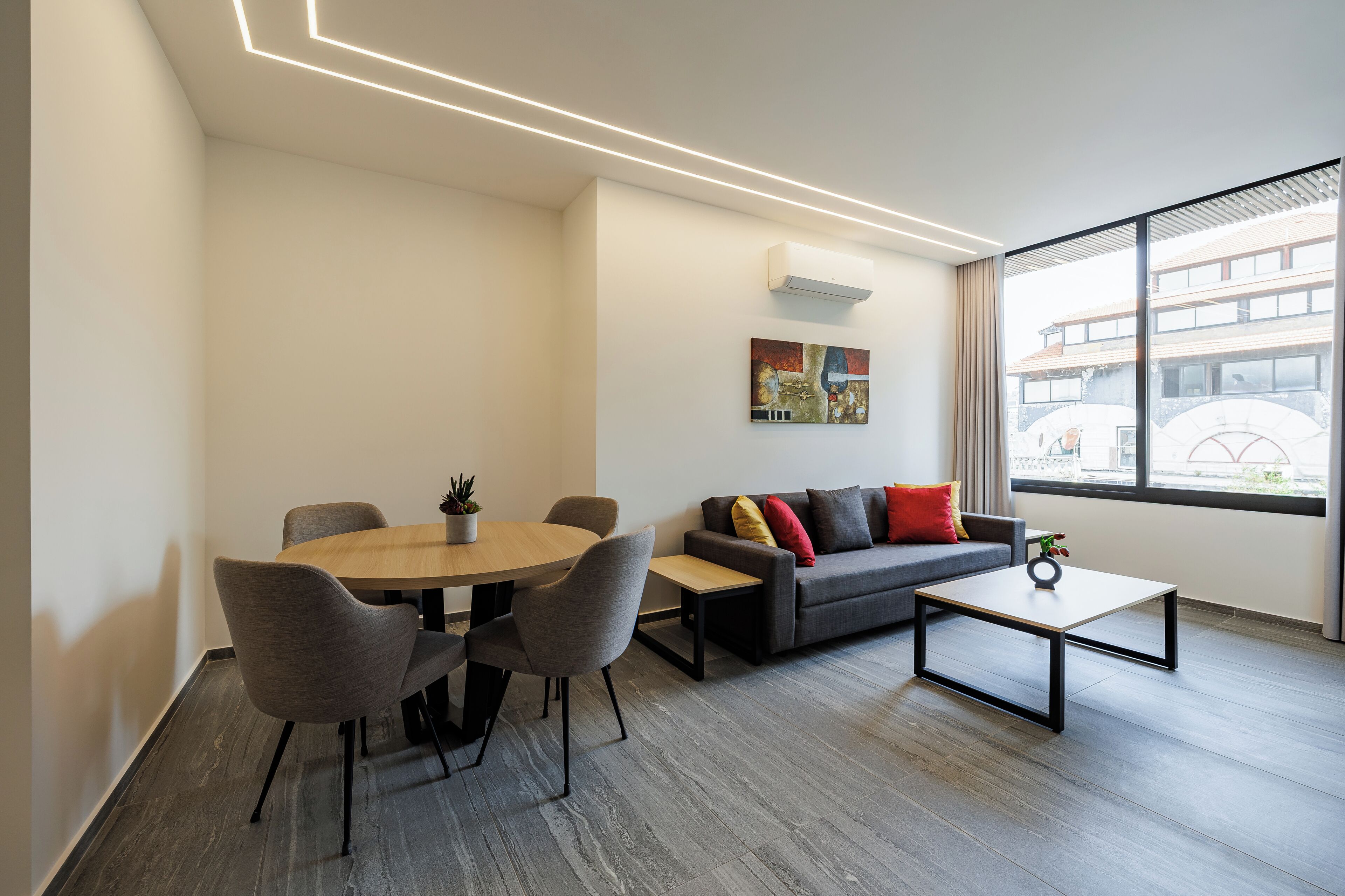 A modern living room with a round dining table, grey sofas, and a coffee table.