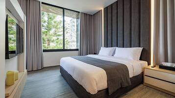 A modern hotel room with a large bed, a bedside table with a lamp, and a view of greenery outside.