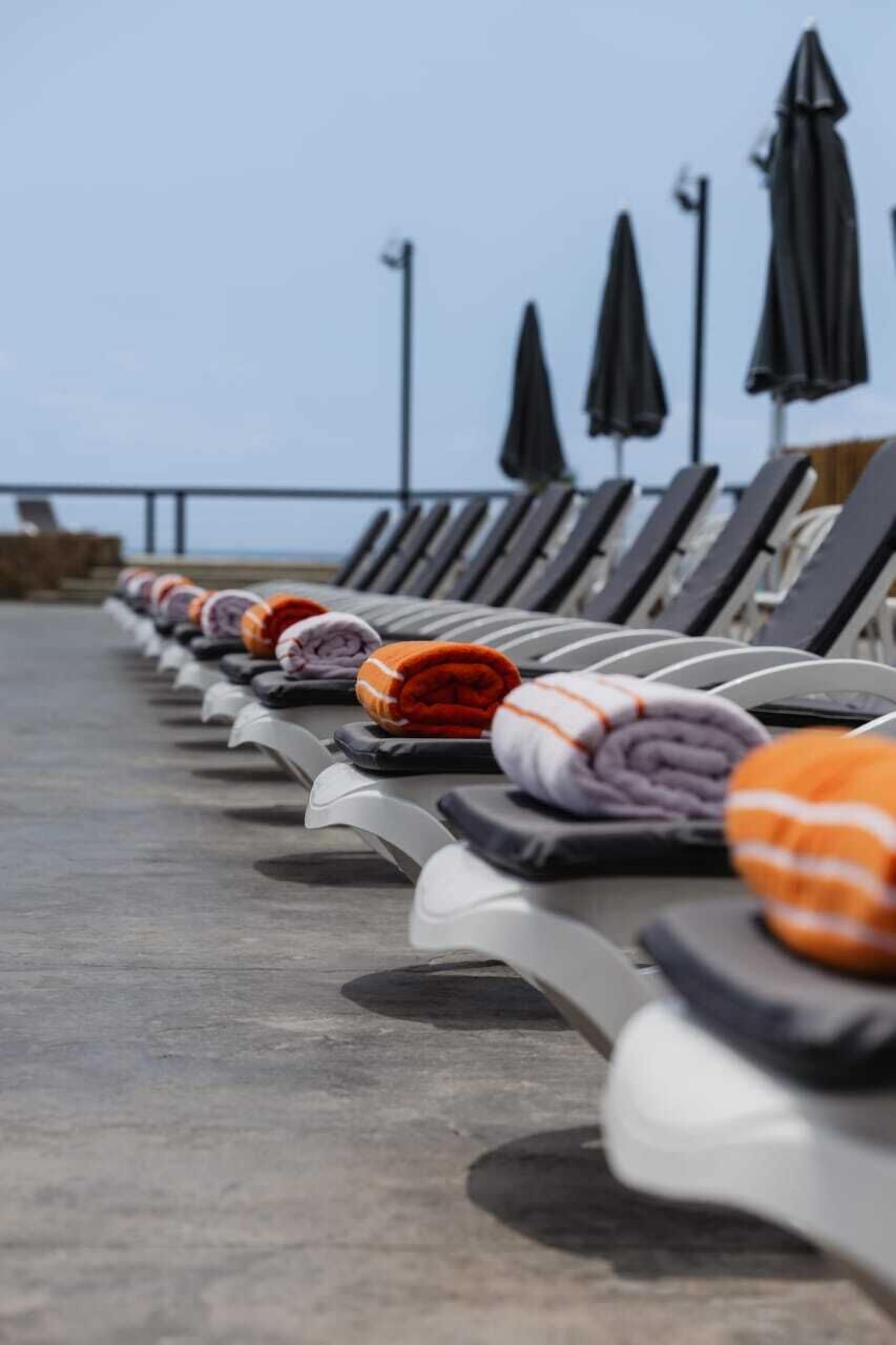 A row of sun loungers with towels, some with orange and white stripes, and black umbrellas.