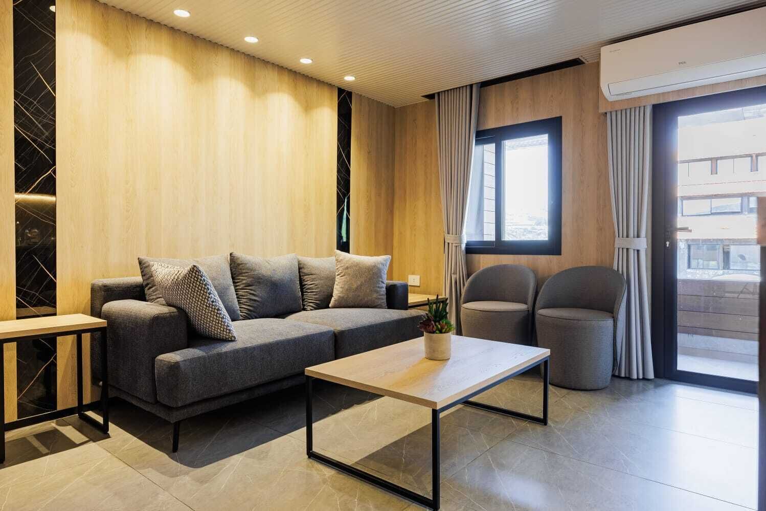 A modern living room with a sofa, two armchairs, a coffee table, and a large window with curtains.