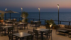 Un patio al aire libre con mesas y sillas, plantas en macetas y vistas al mar.