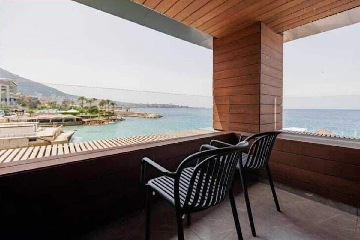 A balcony with two black chairs, a wooden ceiling, and a view of a body of water and distant buildings.