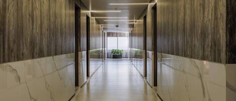 A modern hallway with wooden paneling and marble flooring, leading to a bright area with a plant.