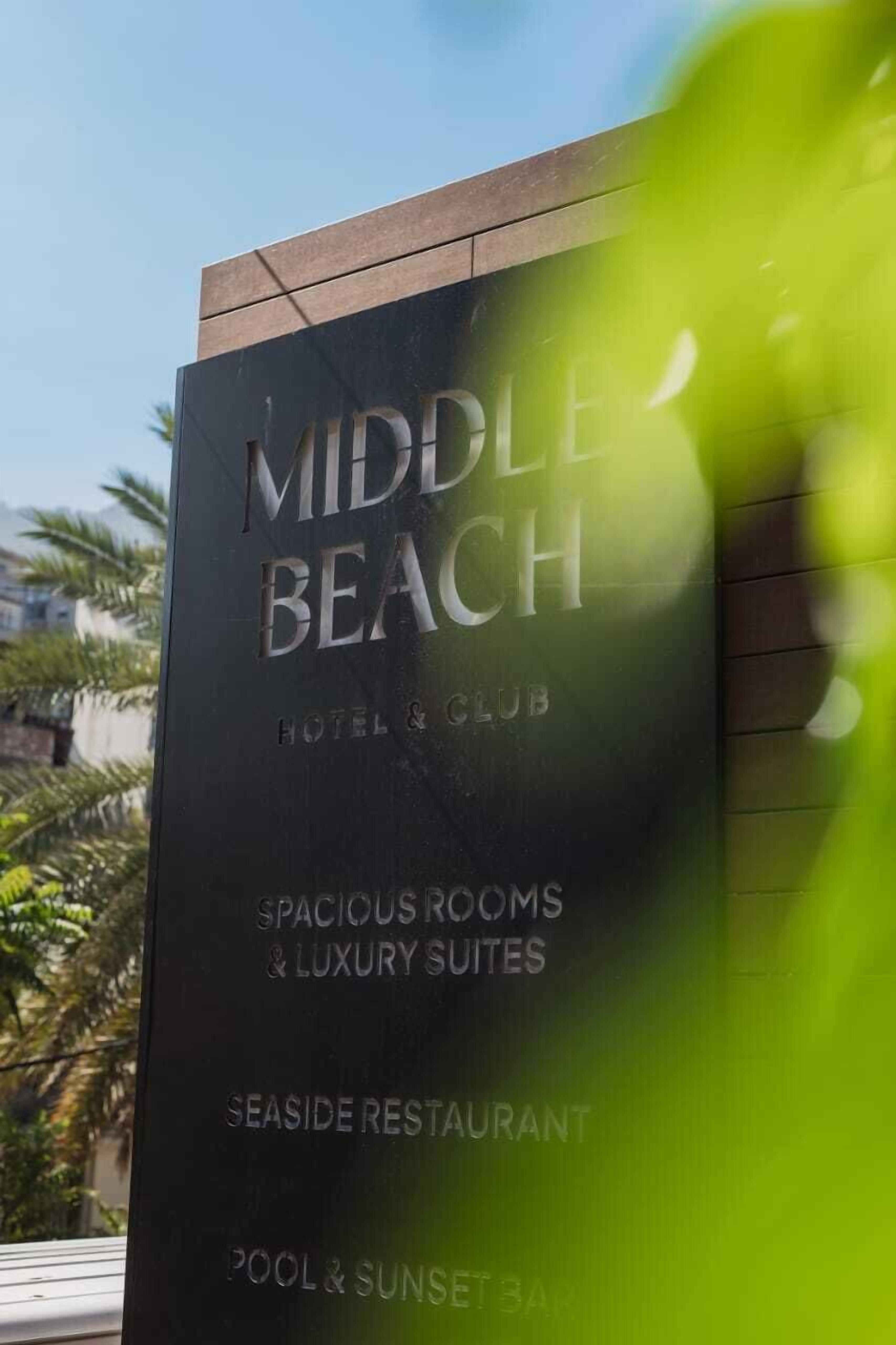 A sign for 'Middle Beach Hotel & Club' highlighting features like spacious rooms, luxury suites, a seaside restaurant, and a pool & sunset bar.